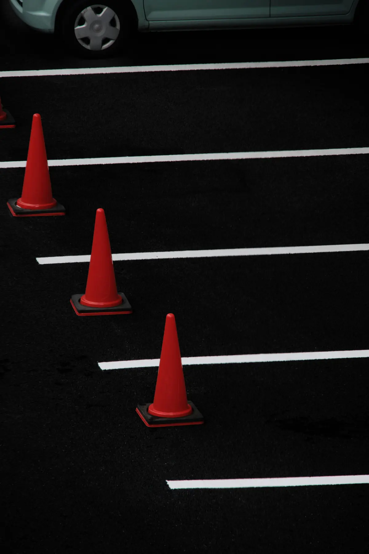 Red traffic cones lined up along the bays of an empty car park.