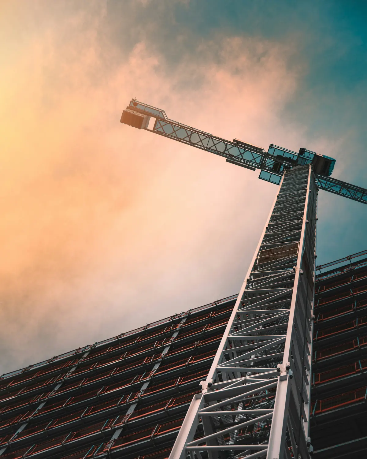 A tower crane rising above a building under construction, seen from below.