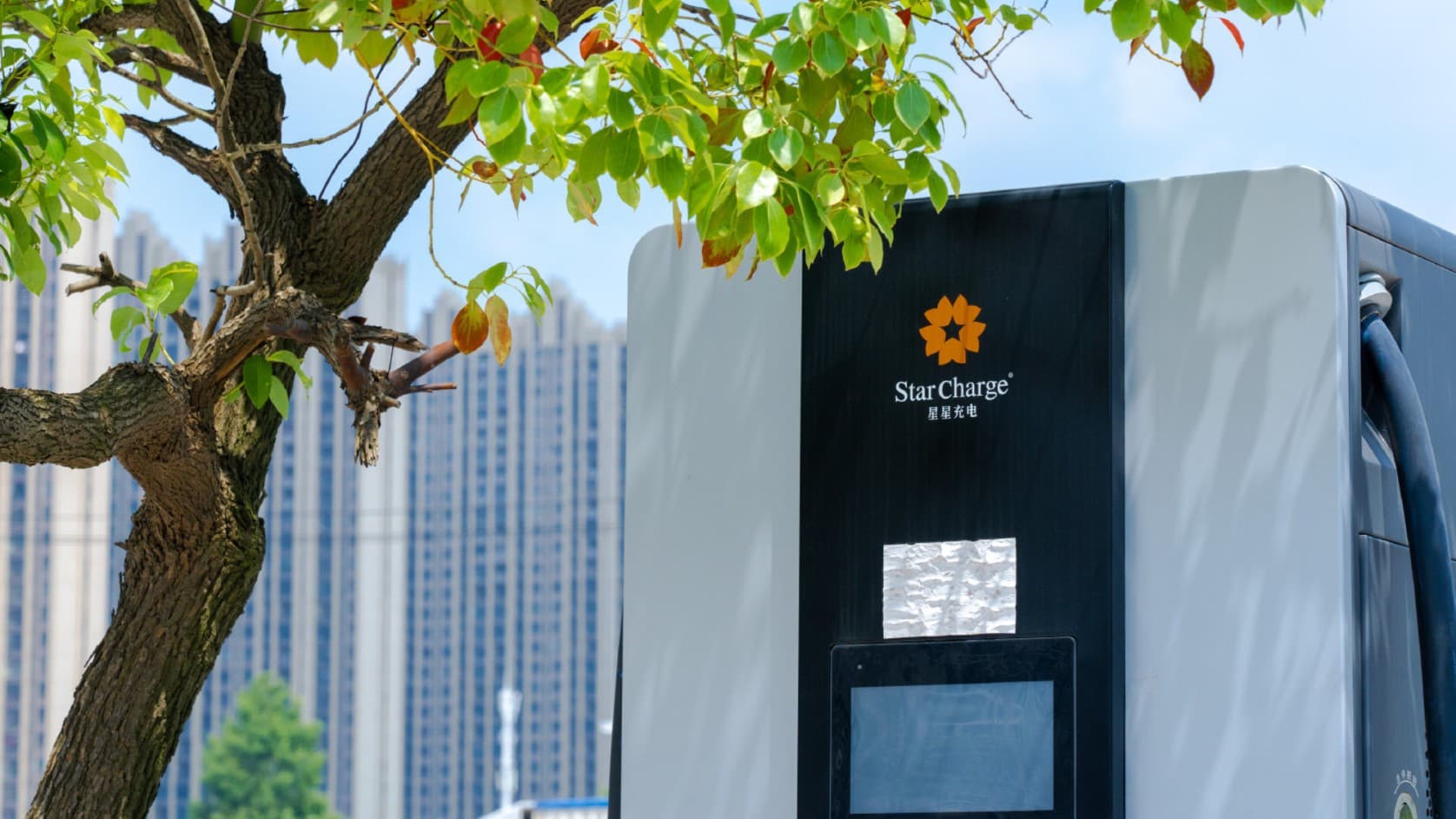 A StarCharge DC charger beneath a tree, with apartment towers behind